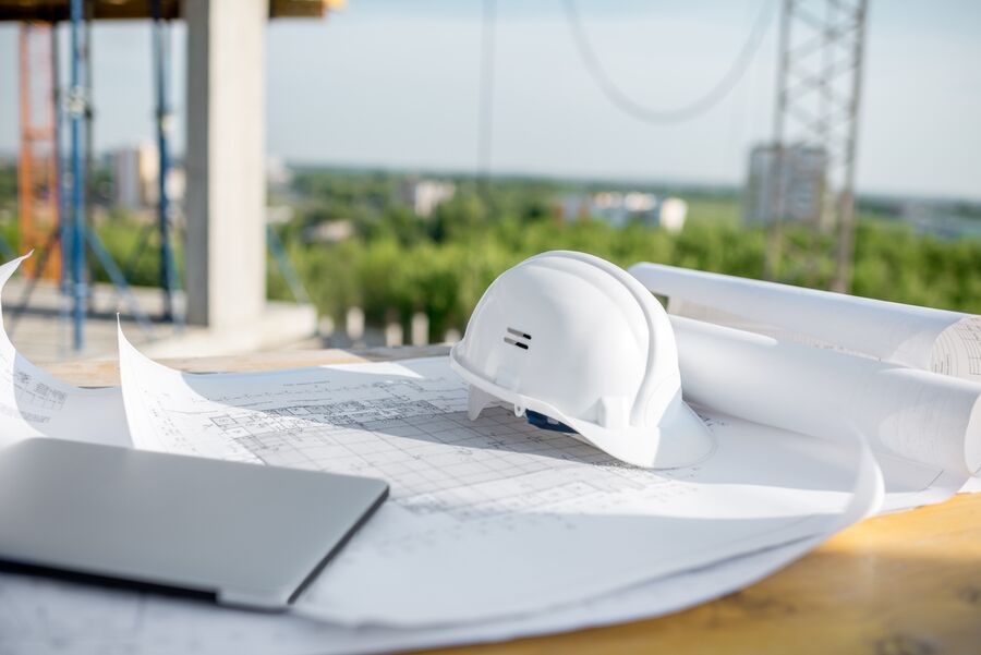 Construction planning documents, hardhat, and laptop for project coordination